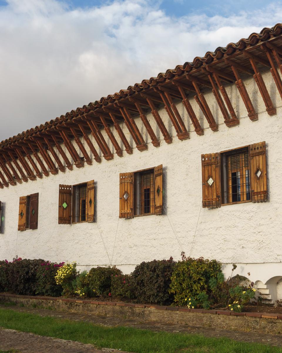 Fachada blanca del Museo del Café en Guatavita, Cundinamarca, con soportes de madera para el techo y ventanas en madera. Fachada blanca del Museo del Café en Guatavita, Cundinamarca, con soportes de madera para el techo y ventanas en madera.