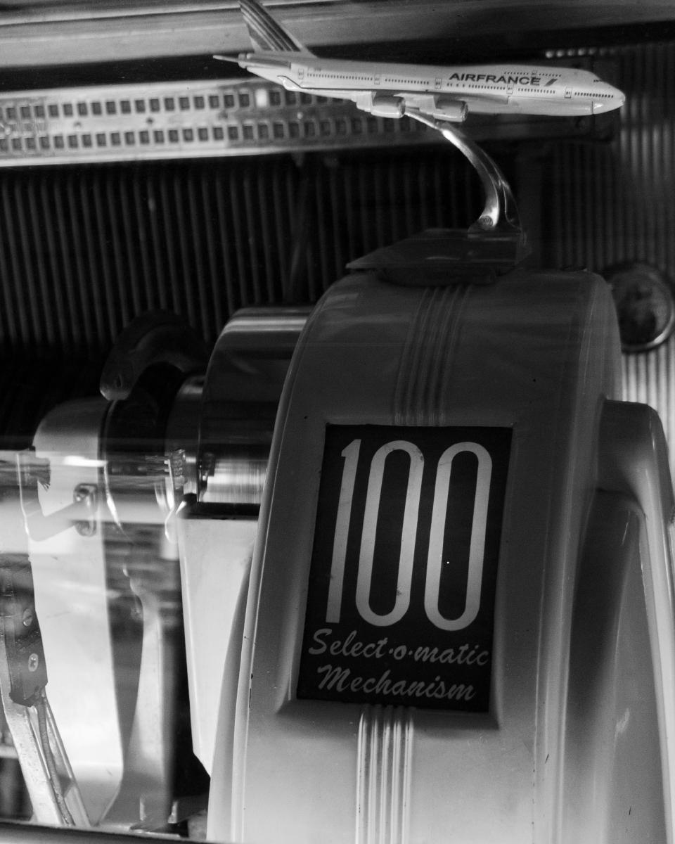 Ventana al interior del tocadiscos, probablemente un Seeburg de la década de los cincuenta. En el mecanismo de reproducción se lee: 100 Select-O-Matic Mechanism. Encima del mecanismo hay un modelo miniatura de un avión comercial de Air France.